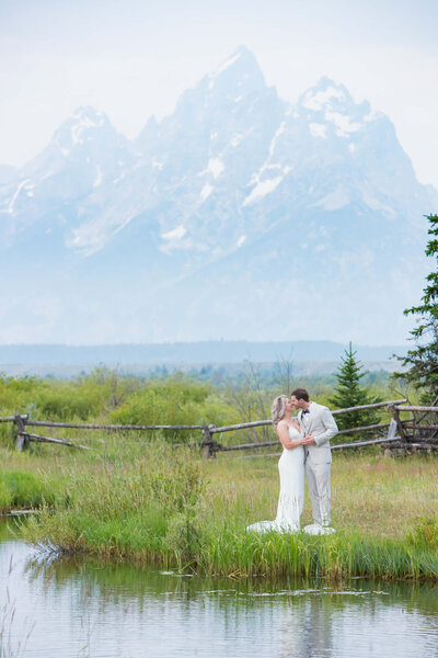 A newlywed couple share a moment in a meadow at Grand Teton National Park with the Grand Teton towering in the background.