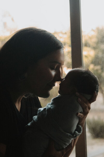 Mother and newborn baby sharing a gentle moment by the window as she holds the baby close.