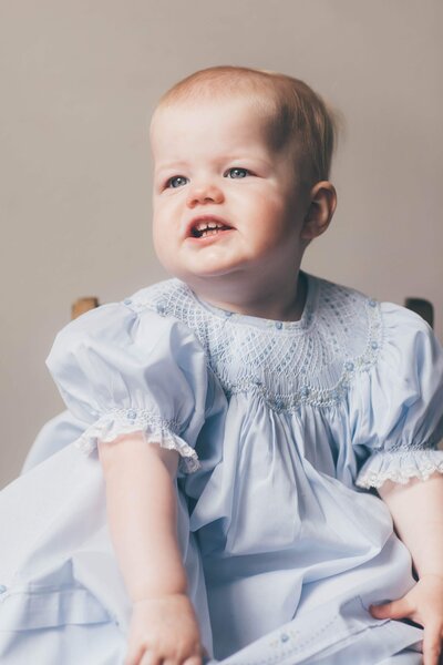 A baby in a lacy blue dress looks off into the distance and smiles captured by family photographer in Shreveport, Britt Elizabeth Photography.