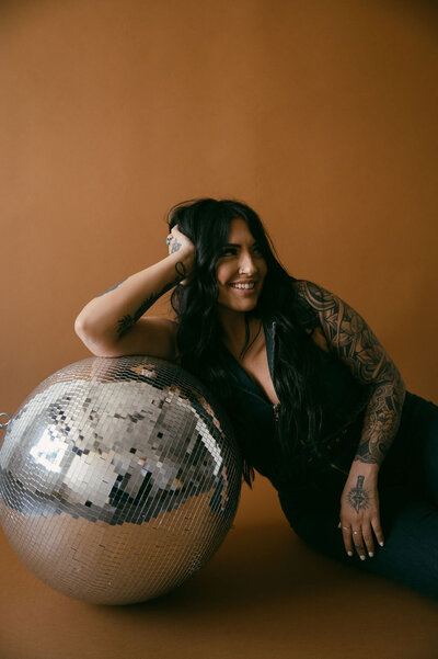 Morgan Rindahl leaning against a large disco ball smailing