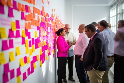 Co-workers looking at sticky notes on a wall.