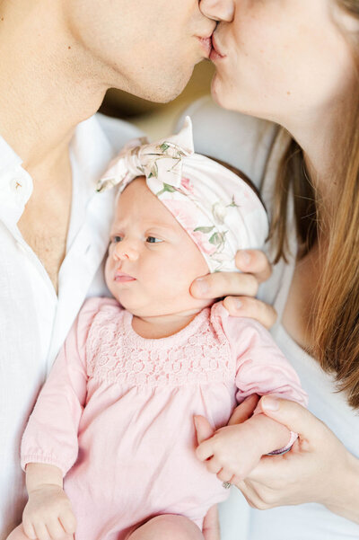 Best Westwood, Massachusetts newborn photographer shot of a newborn baby and her parents kissing above her