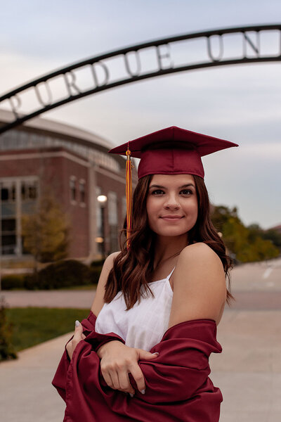 Image of graduate in her cap an gown with her gown shrugged off of her shoulders.