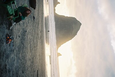 Sara Dobbins sits in green beach chair and smiles at camera in front of Haystack rock