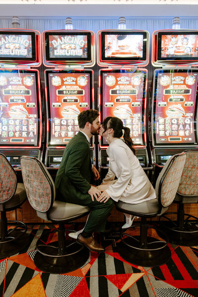 Two people sitting in front of slot machines kissing each other 