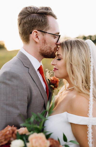 Shenandoah national park wedding photos with groom kissing bride on the forehead of his bride as the sunsets behind them as his bride smailes with her eyes closed captured by charlottesville wedding photographers