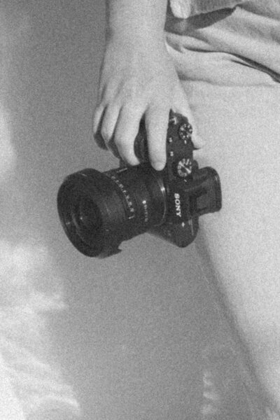 Michaela in a black and white photo holding her camera down to her side with the photo zoomed in on the camera. Branding Photographer in Northeast, TN. 