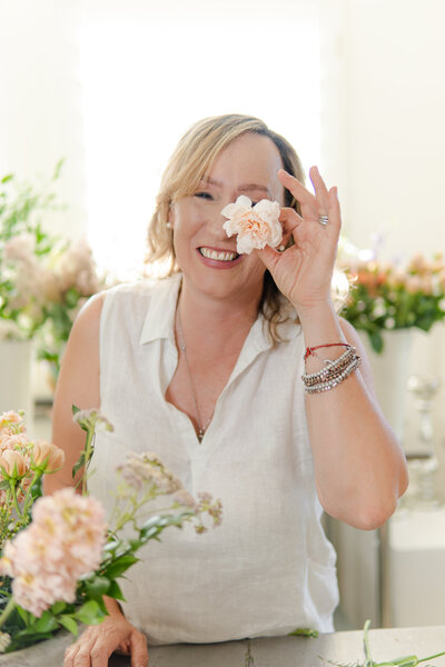 Southern California Wedding Florist Elsa, from Verde Olivo Floral is holding a blush carnation in front of her face and smiling.