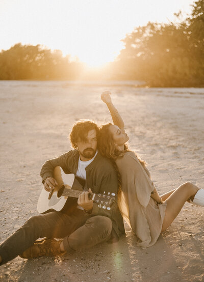 couple sits on sand with guitar