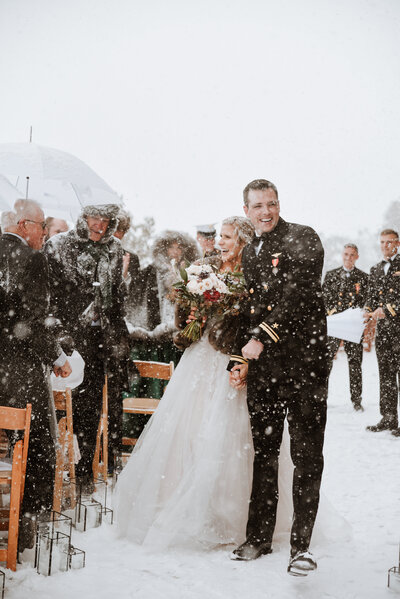 Bride and groom exit snowy aisle beaming with joy after Lodge at Breckenridge mountain ceremony.