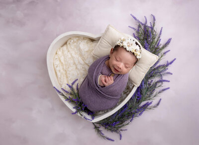 Sleeping newborn swaddled in purple with floral headband, photographed by La Vernia newborn photographer