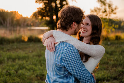 A couple poses for the camera smiling at one another in an open field.