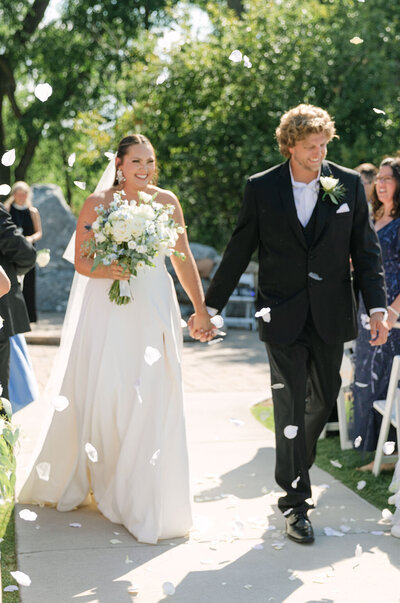 Bride and groom walking down the aisle with flower petals falling — Colorado wedding ceremony exit at Sweet Heart Winery in Loveland.
