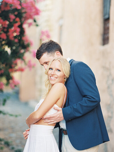 Romantic engagement portrait of a couple embracing along a cobblestone street lined with bougainvillea in the Dominican Republic — captured by Asia Pimentel Photography.