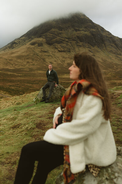 pregnant mother pauses on a rock as husband admires from afar