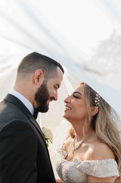 Bride and groom looking and smiling at each other under their veil