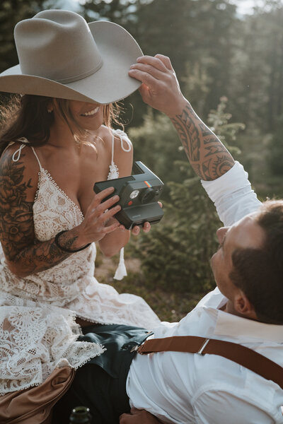 Tattooed couple shares playful moment with Polaroid camera during Breckenridge elopement photo session.