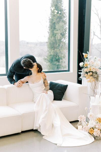 groom leans over the back of the couch to kiss the bride