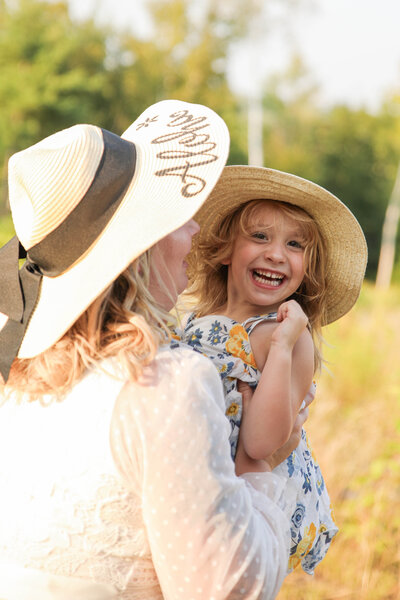 Mom holding daughter who is wearing a hat and smiling | Family Photography Session