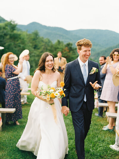 The happy couple holds hands and interacts with guests, as the bride holds the bouquet by Moonlight Floral Co., photographed on film by My Sun and Stars Co.