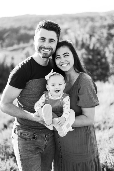 Black and white family photo of a husband, wife, and infant all looking and smiling at the camera in the Brunsummerheide in LImburg