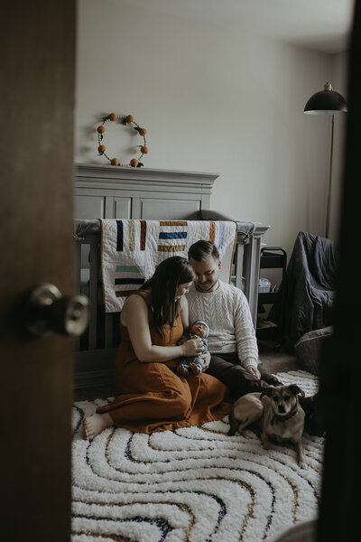 Verona B Photography captures a family sitting on the floor of the baby’s nursery holding their adorable sleeping newborn while the parents gaze tenderly at him. It is such an honor to capture these intimate family moments at an in-home newborn session near Akron, Ohio.