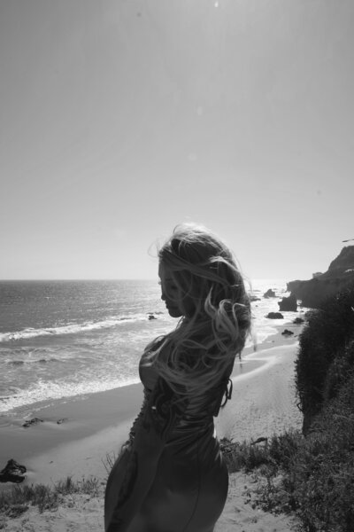 Back view of Nicky Lynn with arms raised on a rocky cliff, symbolizing letting go and self-liberation