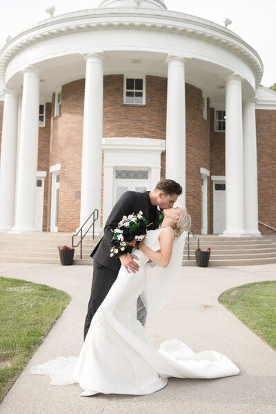 couple kissing while dipping in front of Alma College chapel during their michigan wedding