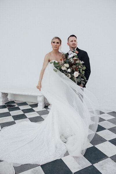 Bride with wind blown veil and groom on chess board flooring