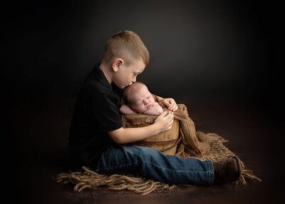 big brother holds baby brother while giving him a kiss on the head.