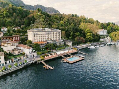A bride in a wedding dress stands in a grand doorway in villa Sola Cabiati, gazing towards a scenic view of mountains and Lake Como. The elegant room features ornate decor, vases, and cushioned benches, capturing the essence of an Italy Wedding Photographer amid the serene outdoor backdrop.