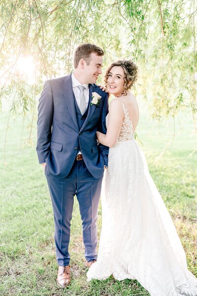 A bride and groom pose for a romantic portrait under a weeping willow tree at golden hour during their wedding at Blue Hill Farm in Northern Virginia