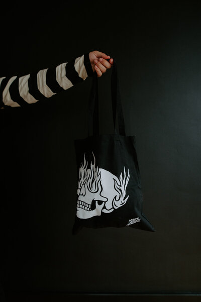 Hand holding a tote bag with a flaming skull graphic
