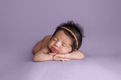 Tacoma newborn photographed on lavender fabric resting on arms small headband no diaper