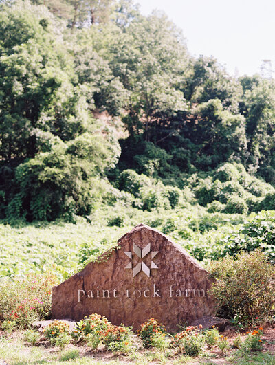 A large rock sign says the name of the property, Paint Rock Farm, with trees in the background of the North Carolina mountains, by film photographer Megan Lynn of My Sun and Stars Co.