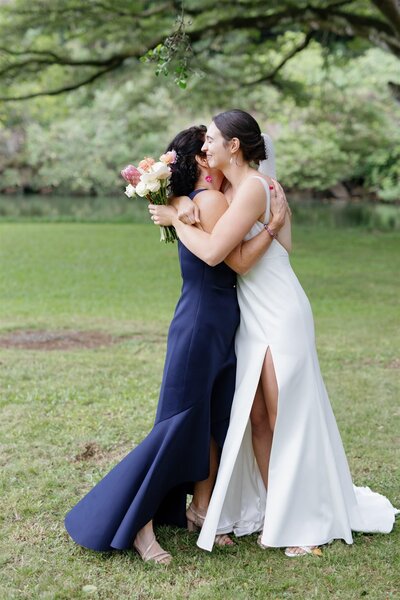 A newlywed in a wedding dress hugging someone in a field 