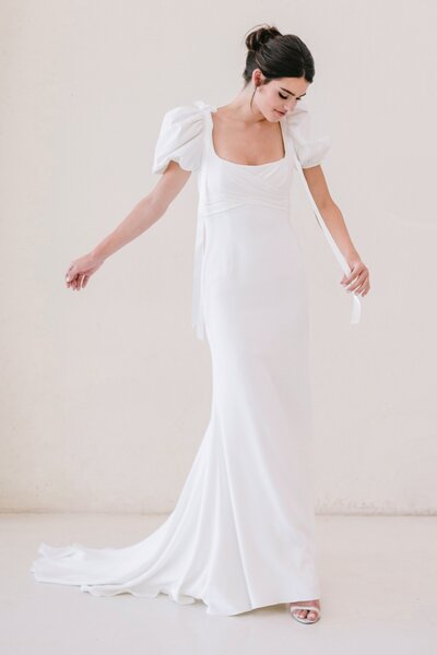 Sculptural, clean, simple and truly bridal. Structured corset with a simple and wearable column skirt featuring a new crepe. Detachable watteau is 22 yards of tulle for added drama, offered dusted with luster pearl details or plain.