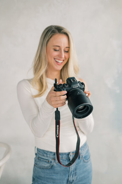 a smiling woman with blonde hair looks at the back of her camera