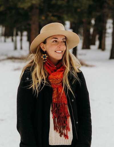 woman standing outside in the snow wearing a hat and red scarf while smiling