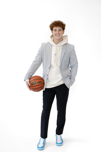 studio portrait of a boy senior high school holding his basketball and wearing a stylish and modern outfit. White backdrop. 