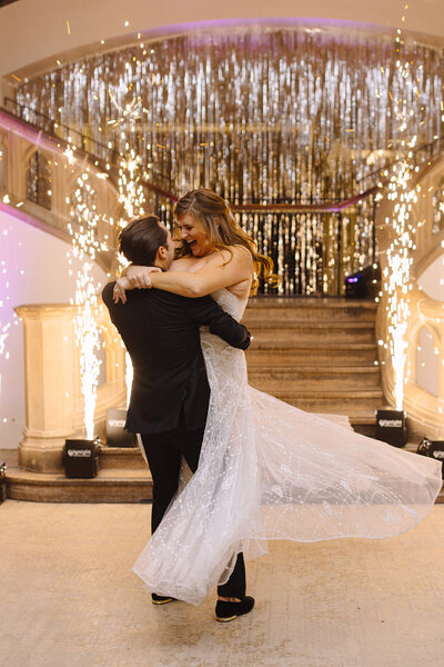 A couple dancing in front of a staircase with indoor fireworks