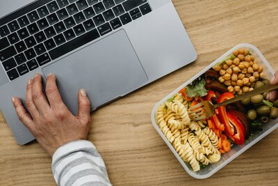 birds eye view of a persons hand on a laptop and eating lunch