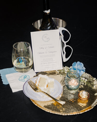 A reception details photograph that shows cake, champagne, candles, an invitation, and custom napkins at a catholic wedding reception in St. Augustine, Florida
