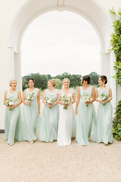 Bridesmaids walk hand in hand under the ceremony arch wearing pale green dresses