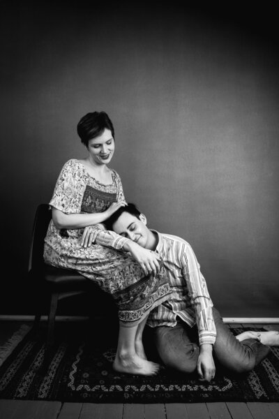 Black and white studio image of a young man with his head resting in his wife's lap, both of them smiling.