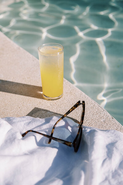 Straw beach tote, earrings and bikini next to luxury pool