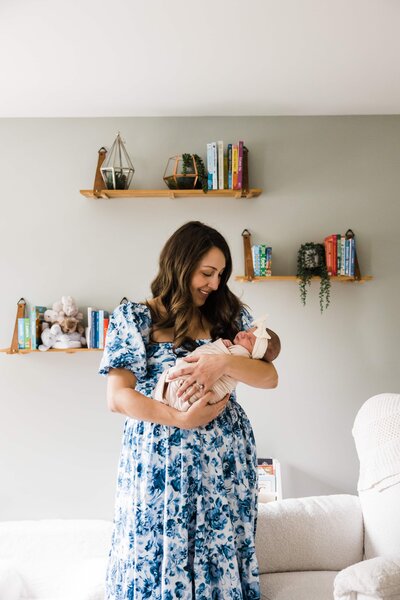Woman in a blue dress lovingly cradling a newborn baby in a bright room, perfectly capturing the essence of at-home newborn photography.