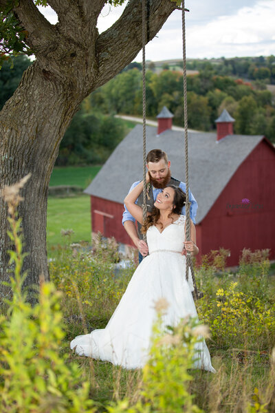 bride on swing infront of groom  with barn  in Wisconsin