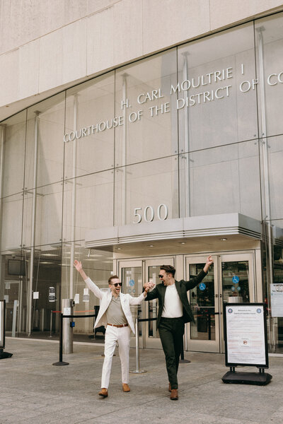 A gay male couple celebrating while walking out of the courthouse after a civil ceremony.