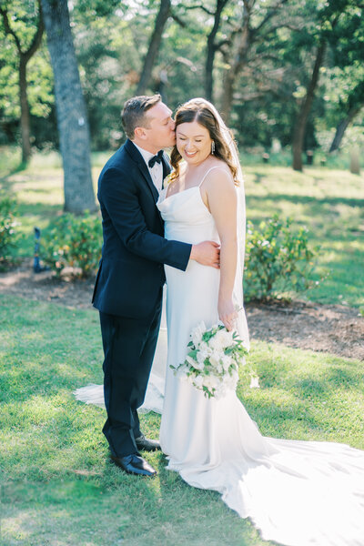 Groom kissing bride on the cheek while she looks down holding her bouquet